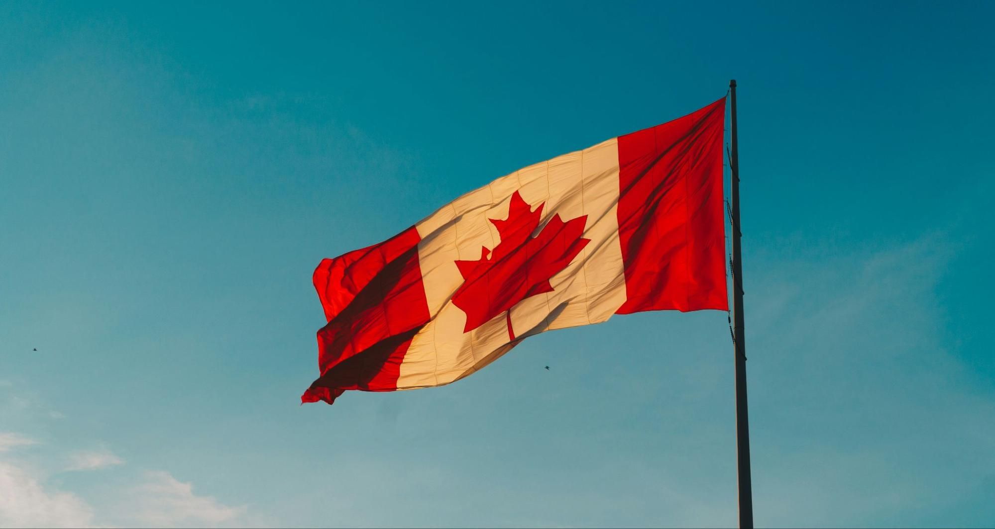 Red and white Canadian flag with maple leaf waving outdoors.