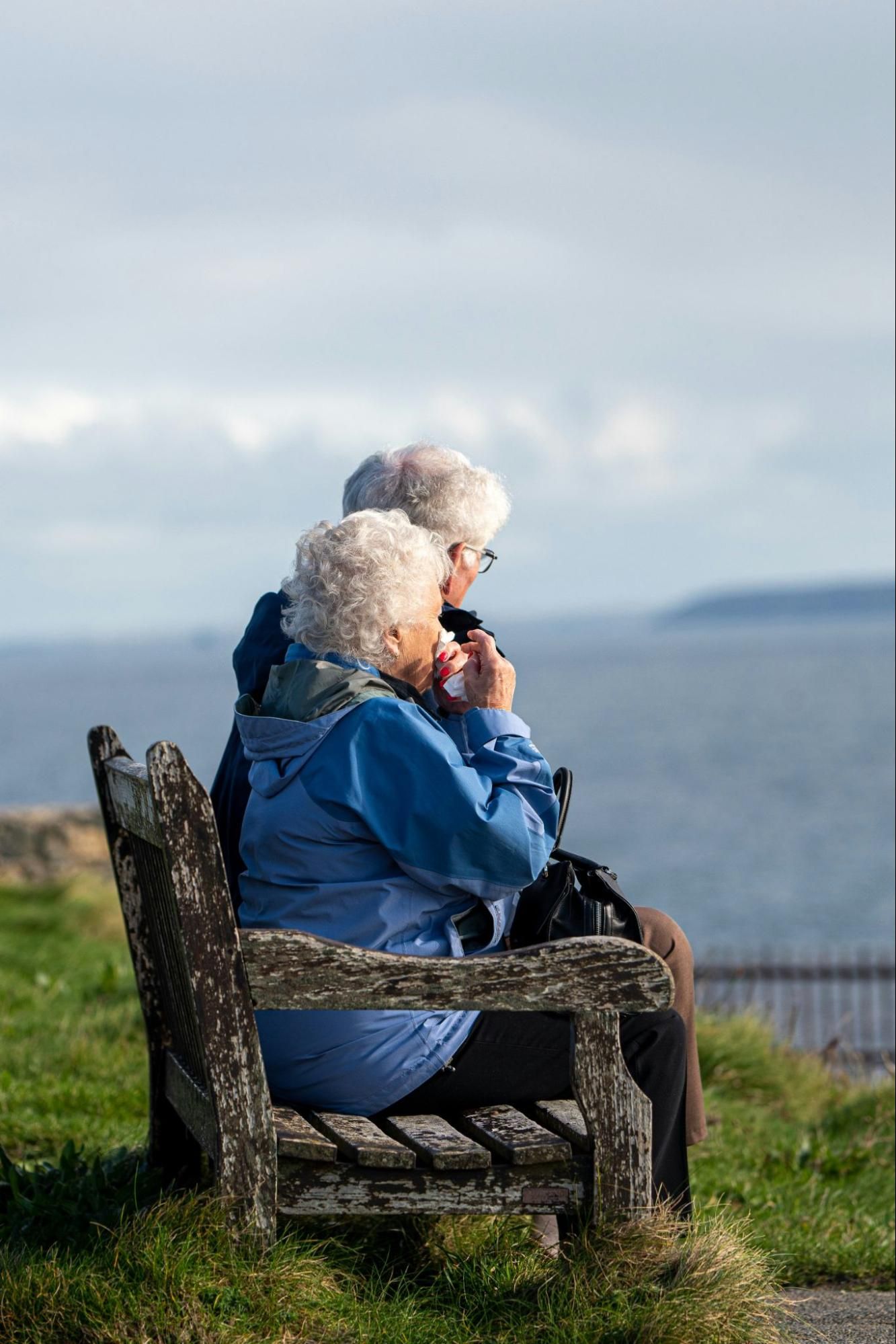 Elderly couple sitting together on a bench outdoors.