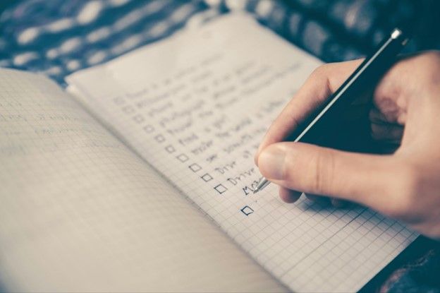Close-up of a hand writing in a notebook with a checkbox list, outlining a detailed plan