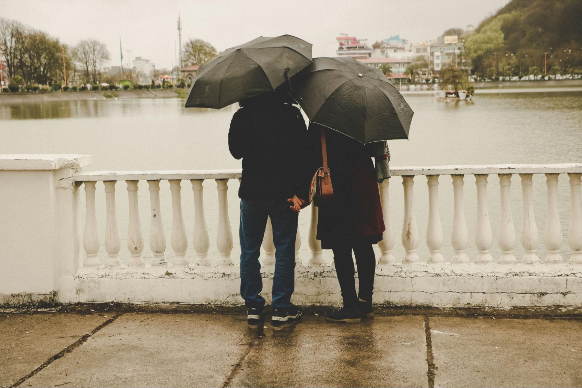 A man and woman holding hands with umbrellas over their heads.