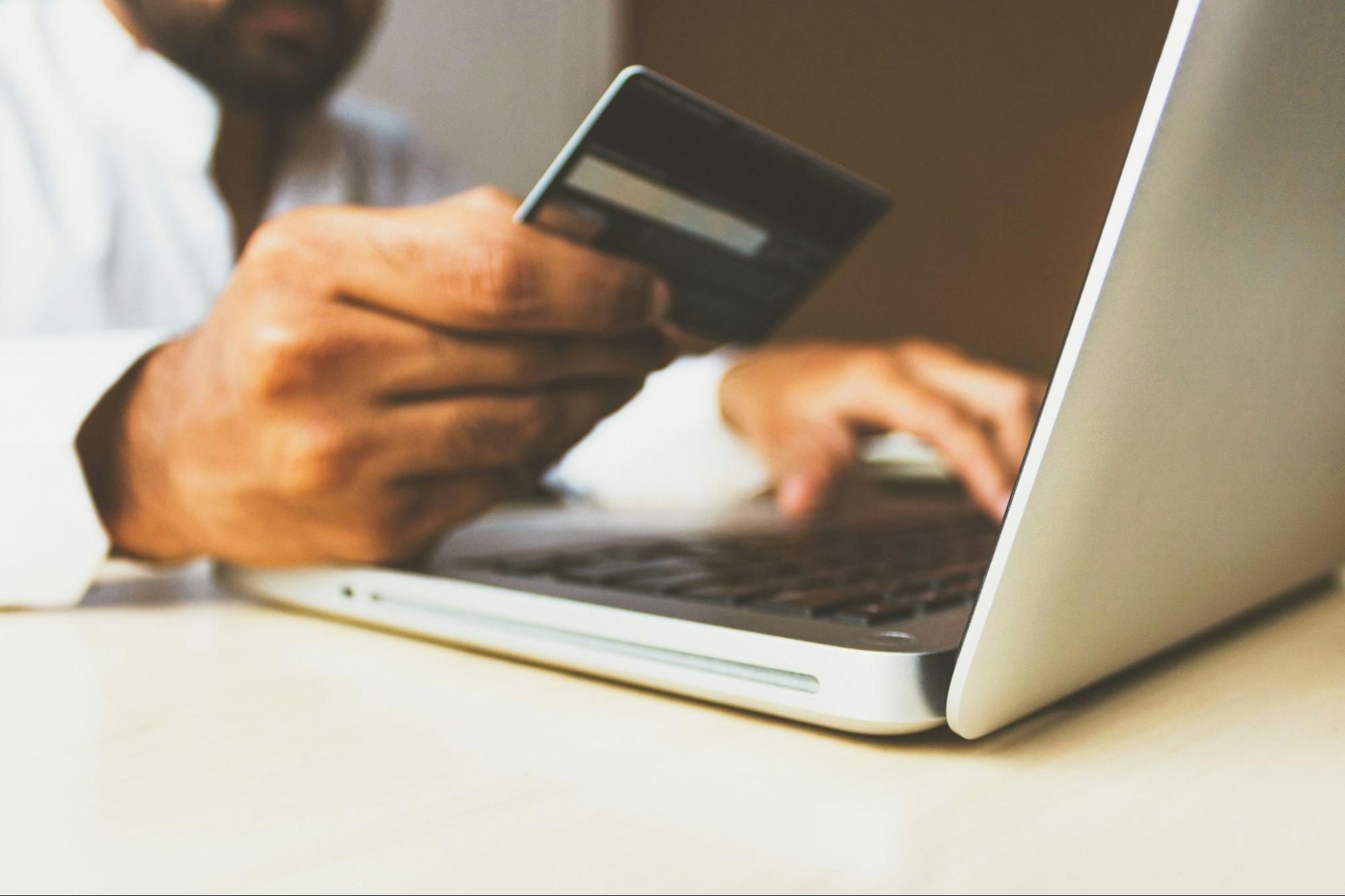 A man sitting at a desk with his laptop, holding a credit card in one hand