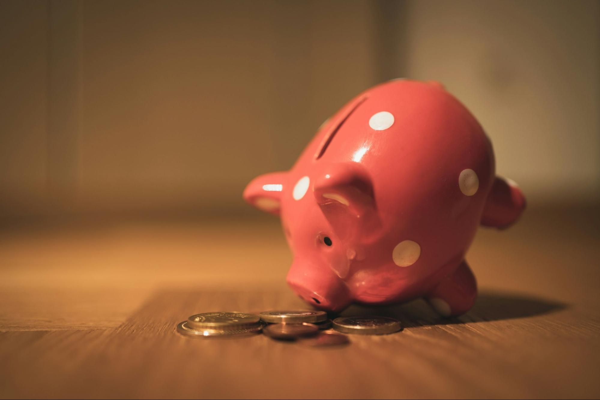 Pink piggy bank tipped forward with its snout in coins