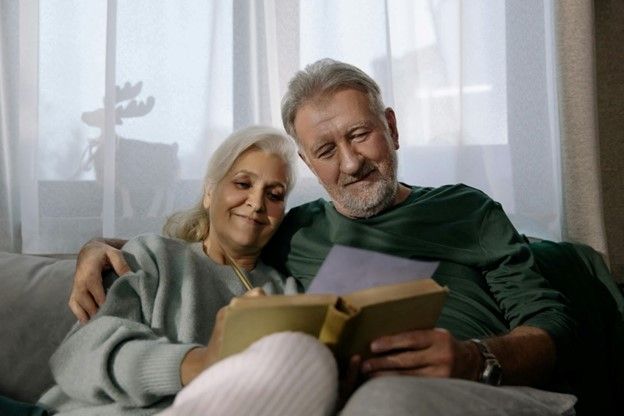 An old man and woman reading a book together, sitting close and enjoying each other's company