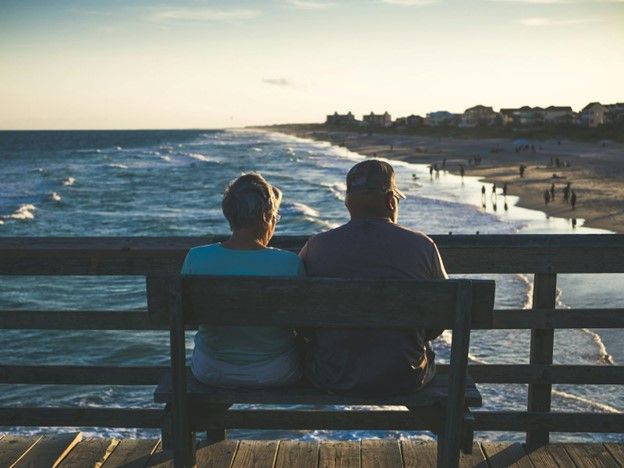 Elderly couple sitting together on a bench, enjoying a peaceful ocean view in retirement.