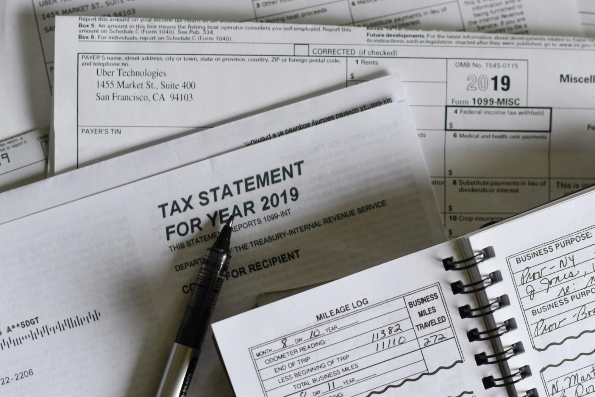 Tax documents laid out with a pen and a mileage logbook.